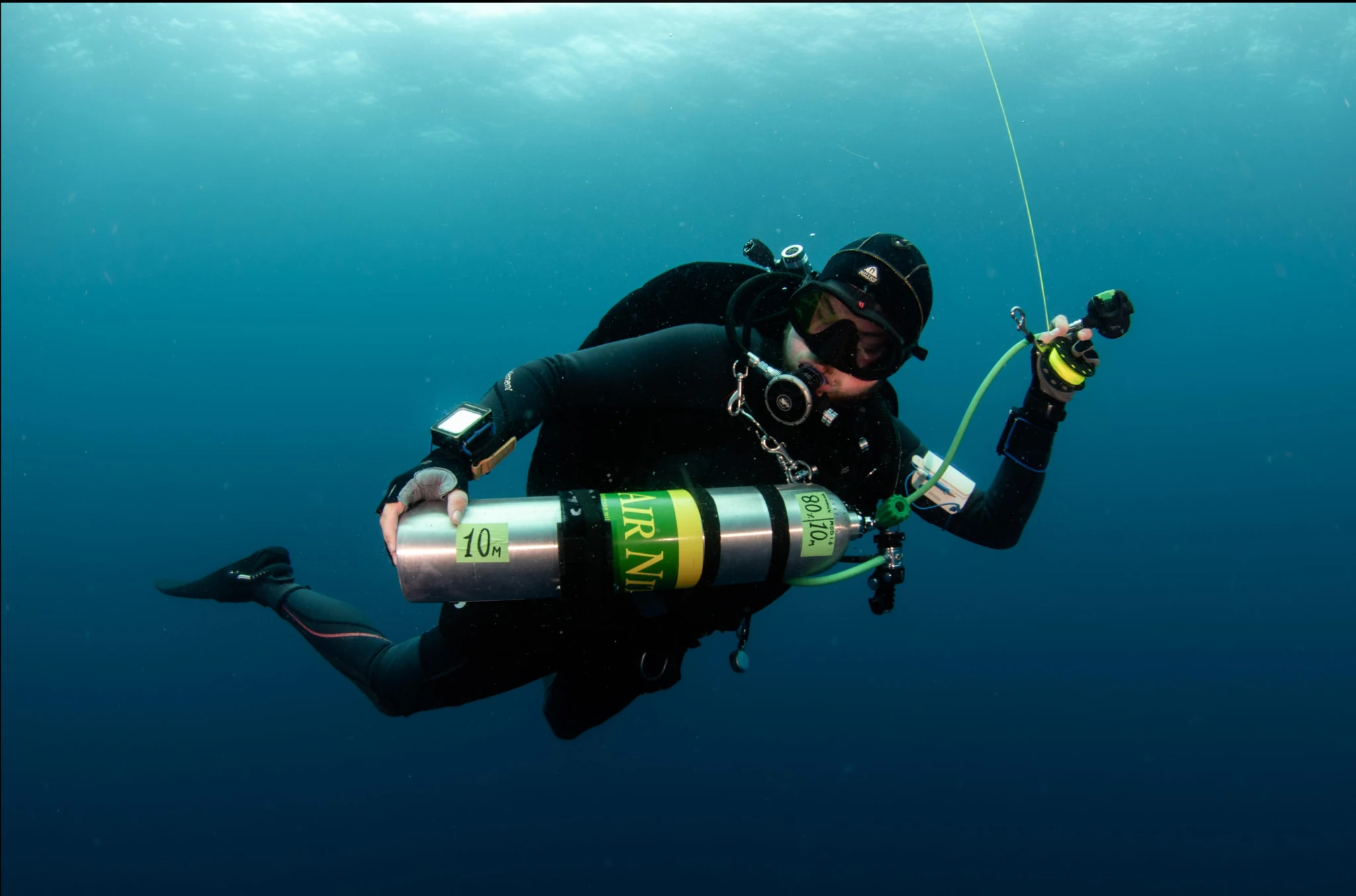 Technical scuba diver underwater carrying an additional cylinder and holding a line