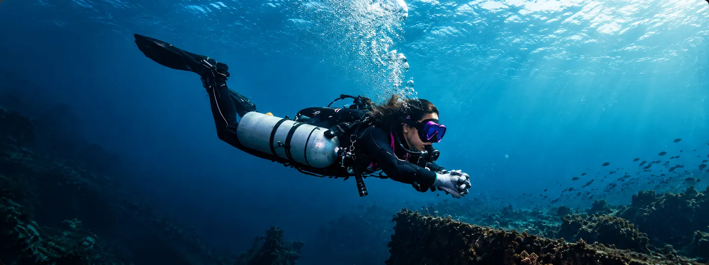 Modern open-water sidemount diver swimming over a sunlit reef.